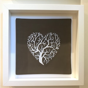 Peut inclure: Un design en forme de cœur représentant un arbre blanc sur un fond brun. Le design est encadré dans un cadre blanc.