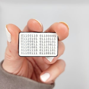 May include: A white enamel pin with a black border featuring a series of binary code: 01100110 0110100001 0111010101 01110111 011000011 01100101 01101011 01110011 01101001 01101111 01101110 01101101 01100111 01100101.
