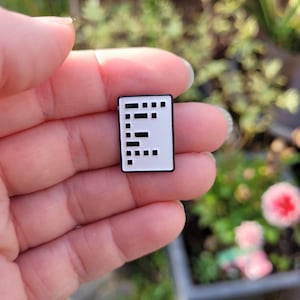 May include: White enamel pin with a black outline, featuring a pixelated letter 'E' design.