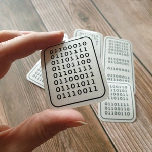 May include: Several white, rectangular stickers with rounded corners, each displaying a black border and a binary code pattern. One sticker is held. The binary code is printed in black on a white background.