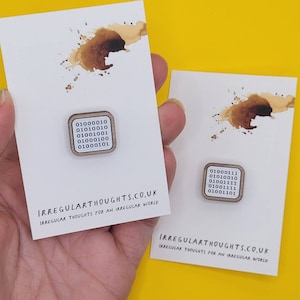 May include: Two square wooden pins with a white background and black text. The text on the pins is binary code. The pins are on white cards with the text "IRREGULARTHOUGHTS.CO.UK" and "IRREGULAR THOUGHTS FOR AN IRREGULAR WORLD".