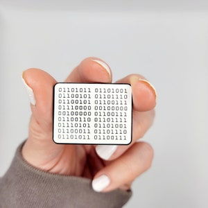 Peut inclure: Une épingle en émail blanc avec du texte noir qui dit "01101011 01101001 01100101 01101110 01100101 01100111 01110000 00100000 00100000 01100111 01100110 01101111 01110101 01101001 01100011 01101110 01101011 01100111".