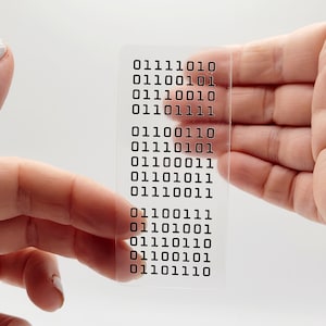 May include: A clear plastic card with a series of binary code printed on it. The code reads: 01111010 01100101 01110010 01110010 01101111 01100110 01110101 01110001 01100011 01100011 01110101 01110011 01100111 01101001 01110110 01100101 01110110 01101110