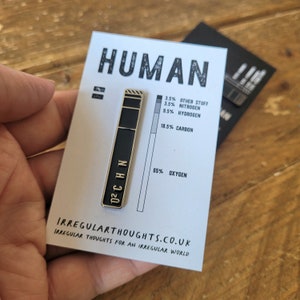 Op de afbeelding: Een witte kaart met het woord "HUMAN" in zwarte tekst. Een zwarte en gouden pin met de chemische formule "O2CHN" is aan de kaart bevestigd. De kaart toont ook een staafdiagram met de percentages van de verschillende elementen die een menselijk lichaam vormen. De tekst op de kaart luidt "3,5% Overig, 3,5% Stikstof, 9,5% Waterstof, 18,5% Koolstof, 65% Zuurstof". De onderkant van de kaart luidt "IRREGULARTHOUGHTS.CO.UK IRREGULAR THOUGHTS FOR AN IRREGULAR WORLD".