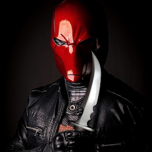 May include: A person wearing a red helmet with a black leather jacket and holding a silver knife.