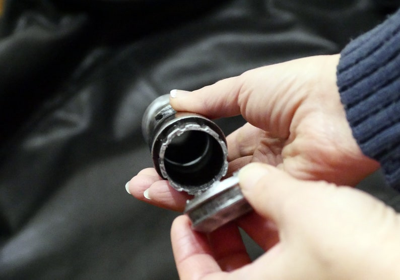May include: A metal bottle stopper with a cylindrical body and a flat, circular top. The stopper is held in a person's hands, with the top partially detached, revealing the interior.