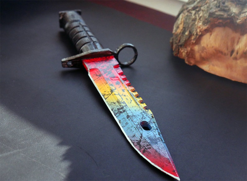 Puede incluir: Un cuchillo de color arco&iacute;ris con mango negro y hoja dentada. La hoja tiene un aspecto desgastado con una pintura de arco&iacute;ris.