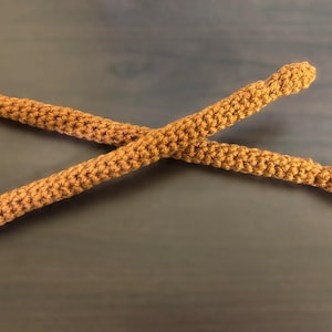 Puede incluir: Dos baquetas de batería de crochet marrón cruzadas.