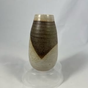 Puede incluir: Un pequeño jarrón de cerámica marrón y blanco con un diseño geométrico. El jarrón mide aproximadamente 15 cm de alto y tiene una abertura estrecha.