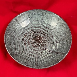 May include: A ceramic bowl with a dark green glaze and a spiderweb design.