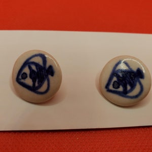 Puede incluir: Un par de pendientes de cerámica blanca con un diseño de pez azul.