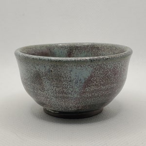Könnte beinhalten: Eine kleine, runde Keramikschüssel mit einem gesprenkelten Überzug in Grautönen, Blau und Lila. Die Schüssel hat einen leicht unebenen Rand und einen abgerundeten Boden.