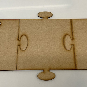 May include: Three unfinished wooden jigsaw pieces that fit together to form a larger rectangle. The pieces are brown in colour and made of smooth wood.