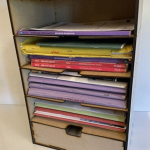 May include: A wooden organiser with multiple shelves and a drawer, filled with various books and papers. The organiser is brown and has a natural wood finish.
