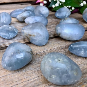 May include: A collection of smooth, light blue celestite tumbled stones. The stones are various sizes and shapes, with some showing natural inclusions.