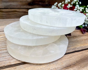 May include: A stack of four circular selenite crystal slabs with a translucent white appearance and a smooth, polished finish. Each slab features a flat top surface and straight, rounded edges, showcasing the natural fibrous texture of the stone.