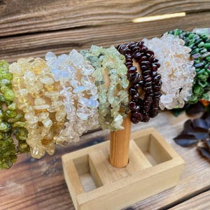 May include: A collection of chip gemstone bracelets in various colors, including green, yellow, white, and red, displayed on a wooden stand. The bracelets are made of small, irregular chips of gemstones.