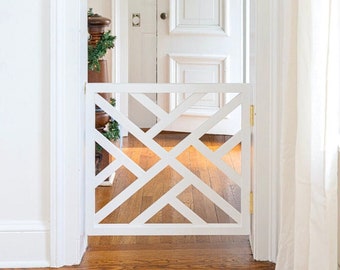 Può includere: Cancello in legno bianco con un motivo a rombi, installato in una porta bianca con pavimento in legno. Una ghirlanda verde è appesa alla porta bianca dietro il cancello.