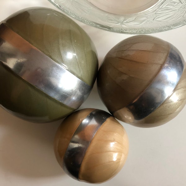 A trio of vintage carpet bowls. 3 ceramic ornamental  balls in warm colours with silver-coloured stripe.  1 small, 1 medium, one large.