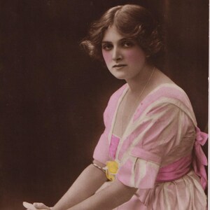 May include: Vintage sepia photograph of Miss Gladys Cooper. She is wearing a pink dress with white stripes and a pink sash. The dress has short sleeves and a bow at the back. The photo is from Dover Street Studios.