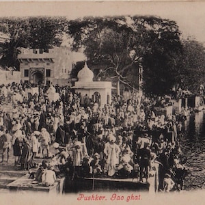 May include: Vintage black and white postcard depicting a large crowd gathered at a ghat, or steps leading to a body of water. Buildings and trees are visible in the background. The text "Pushker, Gao ghat" is printed at the bottom.