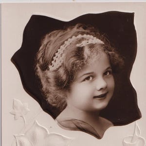 May include: A vintage postcard featuring a sepia-toned portrait of a child wearing a beaded headband. The card includes embossed ivy leaves and the text: A GLAD BIRTHDAY. A LITTLE WISH, A LOVING THOUGHT, A FEW KIND WORDS TO SAY, THAT EVERYTHING YOU CARE FOR MOST MAKE BRIGHT YOUR NATAL-DAY.