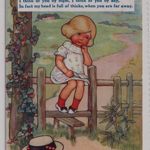 Può includere: Cartolina vintage con il testo "THINKING OF YOU". Raffigura una bambina in abito bianco seduta su una staccionata di legno, con un cappello a terra. Lo sfondo mostra un sentiero e un paesaggio verde.