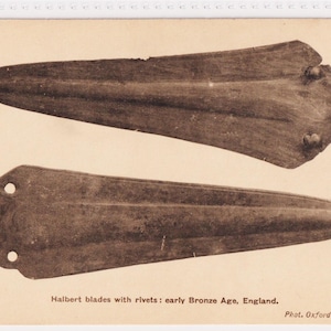May include: Sepia-toned image of two halbert blades with rivets, dating back to the early Bronze Age in England. The blades are elongated with a pointed end and a wider, rivet-studded base. The image is from the British Museum.