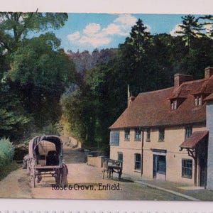 May include: A vintage postcard depicting the Rose & Crown pub in Enfield. The image shows a horse-drawn carriage on a road, passing the pub with its red-tiled roof. The scene is set amidst trees and a blue sky with clouds. The text "Rose & Crown, Enfield" is visible.