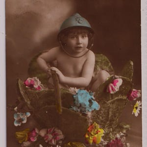 May include: Vintage sepia-toned postcard featuring a child wearing a helmet and holding a stick, seated in a floral arrangement. The text "Graine de Poilu" is written at the top. The image is adorned with colorful flowers.