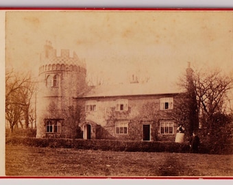 Foto de gabinete británico antiguo de la década de 1880: Pareja victoriana frente a una casa con torre almenada.