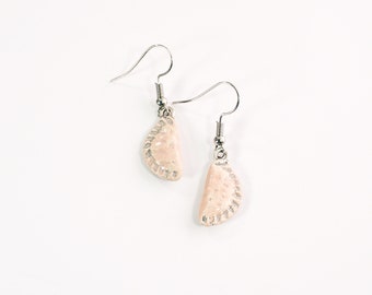 May include: A pair of silver dangle earrings with a light pink, textured, half-moon shaped charm.