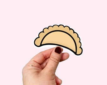 Puede incluir: Una mano sosteniendo una ilustración de dibujos animados de una empanada marrón y beige, un tipo de pastel relleno de ingredientes salados.