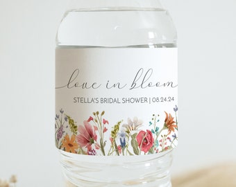 May include: A clear water bottle with a floral label. The label says "love in bloom" and "Stella's Bridal Shower | 08.24.24". The label has watercolour flowers in pink, orange, and purple. Dried flowers are in the foreground.