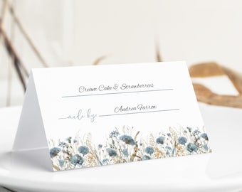 May include: A folded white place card with text that reads "Cream Cake & Strawberries" and "made by Andrea Farron." The bottom of the card features a watercolor floral design in blue and tan. The card sits on a white plate.