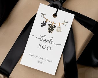 May include: A rectangular white gift tag tied with a black ribbon to a brown paper package. The tag features a clothesline illustration with a bat, a baby onesie, and a ghost, with the text thanks BOO, Karliegh's Baby Shower, and 10.15.