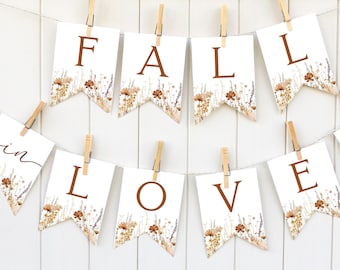 May include: A white banner with brown lettering that reads "Fall in Love" with a floral design. The banner is strung with twine and clothespins.