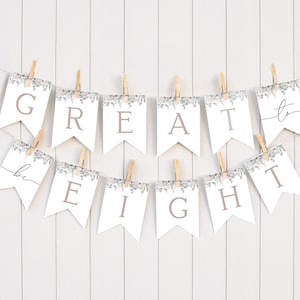 May include: A white banner with the words "be great to eight" in brown text. The banner is decorated with a silver glitter and green foliage pattern. The banner is strung with twine and clothespins.