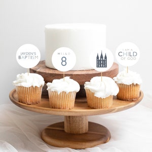 May include: White cupcakes with frosting topped with round paper circles. The circles have text that says "Jayden's Baptism", "Hello 8", a silhouette of a church building, and "I am a Child of God".