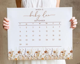 May include: A white calendar with the text "WHEN IS baby due SEPTEMBER" printed in brown. The calendar shows the month of September with the days of the week labeled S, M, T, W, TH, F, S. The numbers 1 through 30 are printed on the calendar. The calendar is decorated with a border of watercolor wildflowers in shades of brown, beige, and purple.