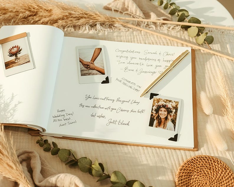 May include: An open wedding guest book with handwritten messages and polaroid photos. A gold pen rests on the page. Dried flowers and decorative elements surround the book, creating a warm, celebratory atmosphere.