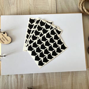 May include: An open scrapbook with white pages, a wooden cover, and a heart-shaped tag that reads "Best wishes from Ukraine!". Several black and white patterned stickers are on the page. Wedding rings are in a wooden box.