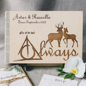 May include: A wooden wedding guest book with engraved deer silhouettes and the word "Always." The book is inscribed with "Artur & Rossella Since September 2023" and "After all this time?" Wedding invitation and RSVP card are visible.