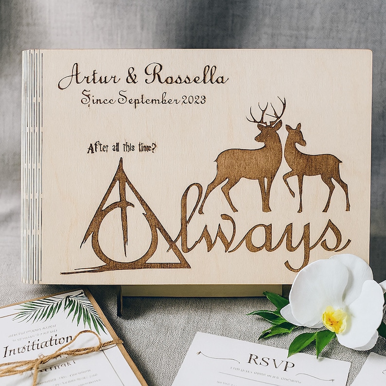 May include: A wooden wedding guest book with engraved deer silhouettes and the word "Always." The book is inscribed with "Artur & Rossella Since September 2023" and "After all this time?" Wedding invitation and RSVP card are visible.