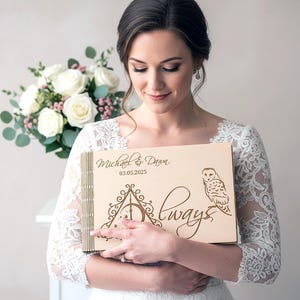 May include: A light-colored wooden wedding guest book with the names "Michael & Dawn" and the date "03.05.2025" engraved on the cover. The design includes an owl and the word "Always" in script. The book is held by a person.