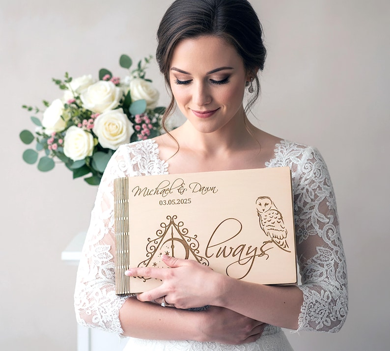 May include: A light-colored wooden wedding guest book with the names "Michael & Dawn" and the date "03.05.2025" engraved on the cover. The design includes an owl and the word "Always" in script. The book is held by a person.