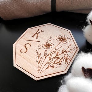 Puede incluir: Un letrero octogonal de madera con las iniciales "K" y "S" separadas por una línea y un diseño floral.