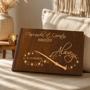 May include: A dark brown wooden book with the names "Cassandra et Quentin" and the word "Always" engraved on the cover. A wand and stars design is also engraved, along with the date "le 15.08.2026".