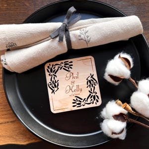 May include: A wooden coaster with a floral design and the text "Phil & Kelly 10/15/2025" engraved on it.