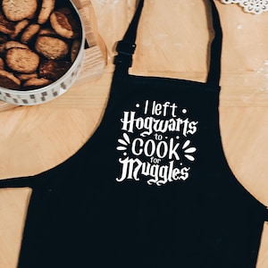 May include: Black apron with white text that reads "I left Hogwarts to cook for Muggles".